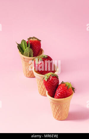 Fragole fresche in tazze waffle su rosa pastello pin-up dello sfondo. Copia dello spazio. Foto Stock
