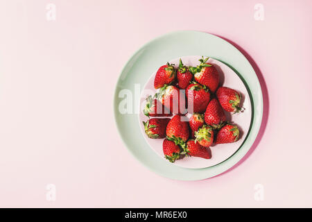 Fragole fresche sulla piastra di turchese su rosa pastello pin-up dello sfondo. Copia dello spazio. Vista superiore Foto Stock