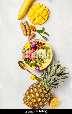 Mango banana ananas curcuma colazione frullato superfoods ciotola guarnita con frutta, bacche e semi. Tettuccio di vista superiore laici piatta Foto Stock