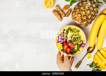 Mango banana ananas curcuma colazione frullato superfoods ciotola guarnita con frutta, bacche e semi. Tettuccio di vista superiore laici piatta Foto Stock