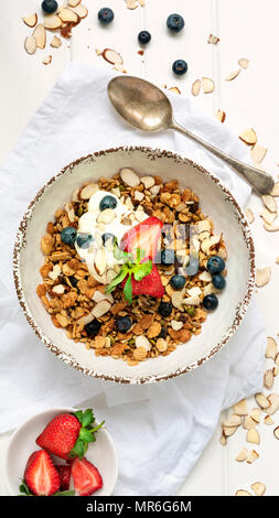 Ciotola di muesli, fragole, mirtilli, slithered mandorle e yogurt con un cucchiaio. Foto Stock