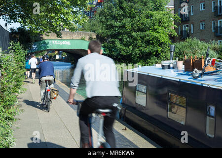 Per gli amanti del jogging jogging e pendolari in bicicletta a Rush Hour passato un narrowboat sul Regent's Canal in Haggerston, East London, Regno Unito, su una serata primaverile Foto Stock