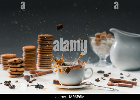 La canna da zucchero Zollette di zucchero spruzzi in tazza calda con caffè nero nella parte anteriore di biscotti e spezie Foto Stock