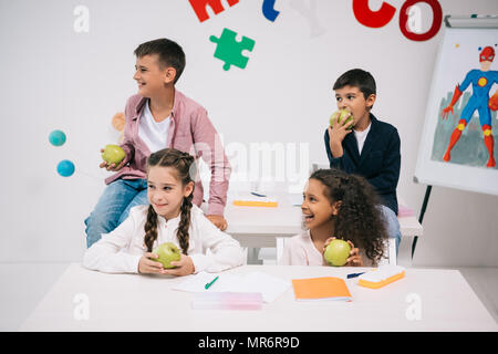 Gruppo multietnico di bambini a mangiare le mele durante la seduta in Aula durante la pausa Foto Stock