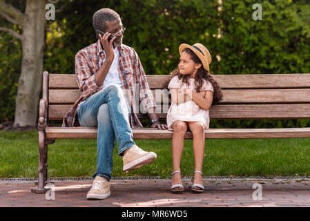 African American nipote con bracci incrociati cercando sul suo nonno parlando sullo smartphone in posizione di parcheggio Foto Stock