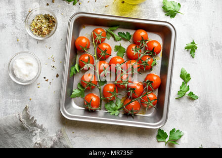 Cotta nel forno i pomodori ciliegia nel vassoio da forno su sfondo di pietra. Vista superiore, laici piatta Foto Stock