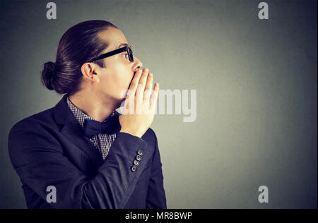 Giovane uomo che copre la bocca mentre spettegolare e raccontare segreti in sussurro. Foto Stock