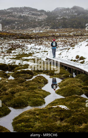 Un escursionista non identificato si riflette nell'acqua accanto al sentiero presso il Cradle Mountain National Park in una giornata invernale in Tasmania Australia Foto Stock