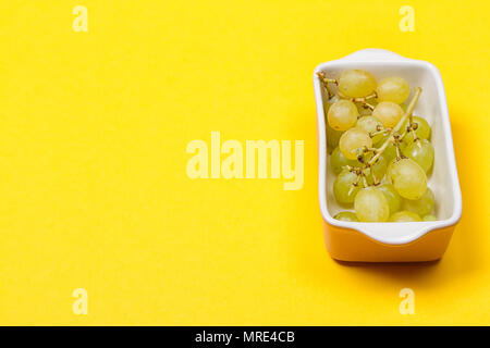 Le uve in un vaso di ceramica su sfondo giallo. Uva verde Kis Mish. Vista dall'alto. copy-spazio Foto Stock