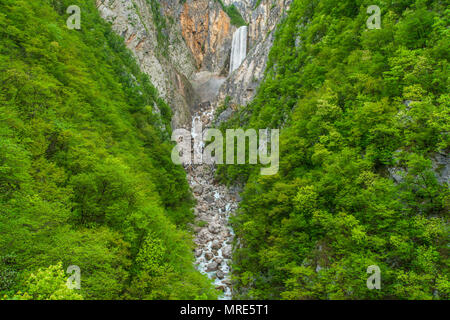 Inquadratura simmetrica di imponente cascata a cascata verso il basso ripidi pendii rocciosi, incorniciato da un rigoglioso bosco, bosco verde da abbondante acqua a primavera. Foto Stock