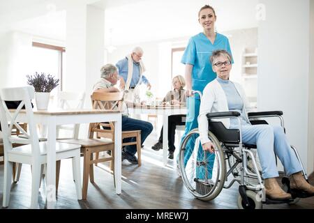 Senior donna in sedia a rotelle con cura lavoratore nella casa di cura. Foto Stock