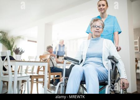 Senior donna in sedia a rotelle con cura lavoratore nella casa di cura. Foto Stock