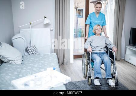 Senior donna in sedia a rotelle con cura lavoratore nella casa di cura. Foto Stock