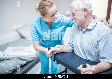 Senior uomo utilizzando rollator con cura lavoratore assistere. Foto Stock