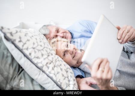 Coppia senior sdraiato a guardare digitale compressa. Foto Stock