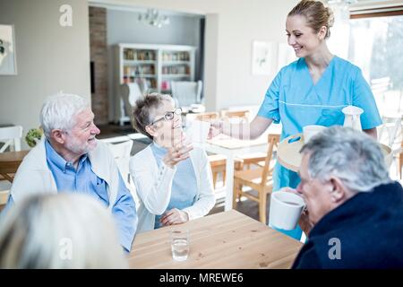 Lavoratore di cura che serve tè al senior donna nella casa di cura. Foto Stock