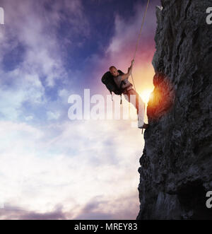 Uomo si arrampica un pericolo di alta montagna con una corda durante il tramonto Foto Stock