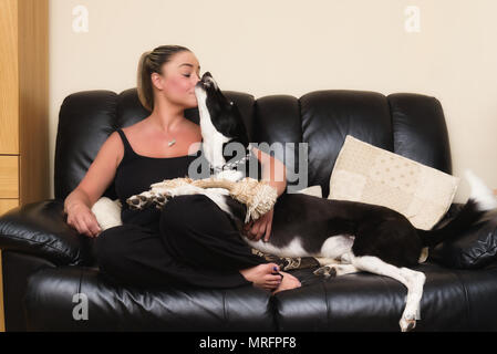 Donna felice baciato dalla sua Black & White cane sul divano di casa in soggiorno Foto Stock