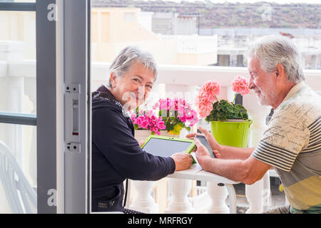 Adulto coppia senior utilizzare laptop outdoor le attività per il tempo libero presso la terrazza a casa. Il sorriso e godersi il bel tempo e la vita in pensione per stare insieme Foto Stock