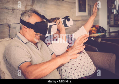 Senior l uomo e la donna con gli occhiali di protezione auricolare di realtà virtuale occhiali di giocare e divertirsi seduti sul divano di casa. Filtro a caldo e la vita insieme c Foto Stock