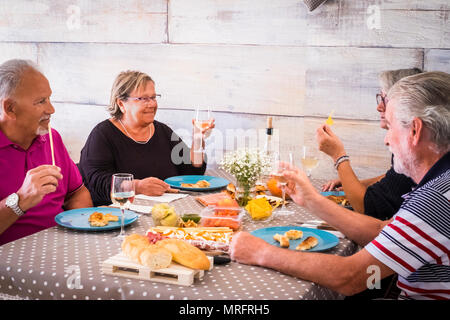 Due coppie di persone mangiare insieme a casa durante il giorno. insieme le attività per il tempo libero interne matura per uomini e donne adulti con i capelli bianchi. sorriso e en Foto Stock