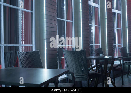 Tavoli e sedie in night cafe contro lo sfondo di una finestra con una tazza di caffè sotto Foto Stock