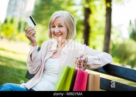 Adulto felice donna seduta nel parco dopo lo shopping. Foto Stock