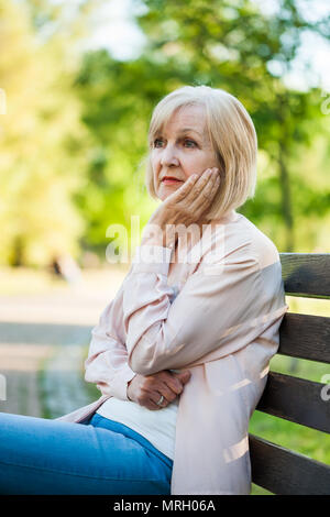 Lonely adulto donna seduta in parco nella disperazione. Foto Stock