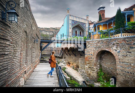 Tourist donna in giacca marrone passeggiando per le vecchie strade di pubblico bagno solforico quartiere centrale di Tbilisi, Georgia Foto Stock