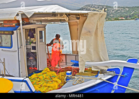 Pescatore greco riassettavano le reti a bordo la sua piccola barca nel porto della capitale Argostolis in Kefalonia / Cefalonia Grecia Foto Stock