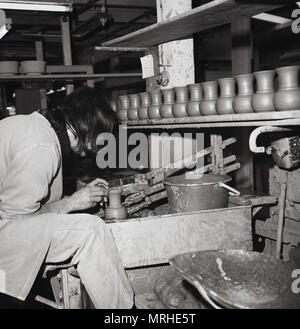 Anni sessanta, foto storiche di un artigiano o artigiano al lavoro, un maschio di argilla all'interno del potter la sua officina rendendo in ceramica a mano utilizzando una meccanica tornio del vasaio per forma o gettare l'argilla, England Regno Unito. Foto Stock