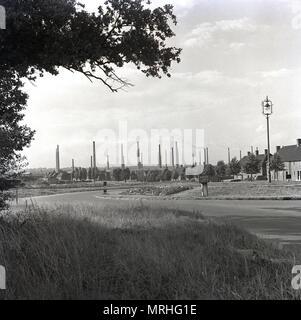 Degli anni Cinquanta, storico vista attraverso un campo che mostra le ciminiere della London Brick Company, Stewartby, Bedfordshire, Inghilterra, Regno Unito. I laterizi erano a casa per il più grande del mondo di forno e accanto al gigante sito industriale, era un 'modello 'villaggio costruito per alloggiare gli operai della fabbrica. Originariamente una zona agricola denominata Wootton Pillinge, è stato rinominato "tewartby' nel 1937 dopo la famiglia Stewart che ha creato i laterizi. Foto Stock