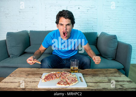 Felice caucasico giovane tifoso celebrando a guardare la sua squadra di calcio di segnare un gol mentre si guarda a casa sul suo lettino. Foto Stock