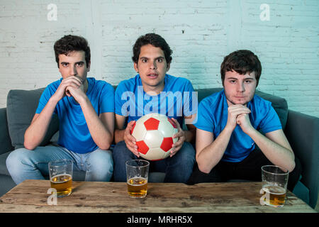 Giovane gruppo di soggetti di razza caucasica Tifosi delusi a guardare una partita di calcio sul lettino. Foto Stock