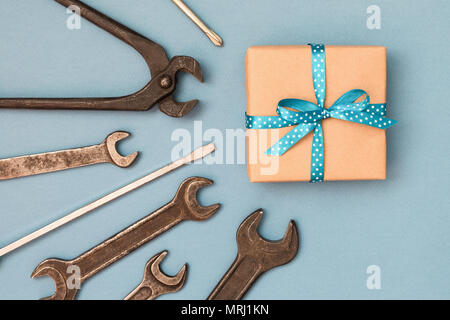 La festa del papà concetto card con il lavoro dell'uomo strumenti su sfondo grigio e confezione regalo avvolti in carta kraft e legato con la prua blu. Vista dall'alto. Foto Stock