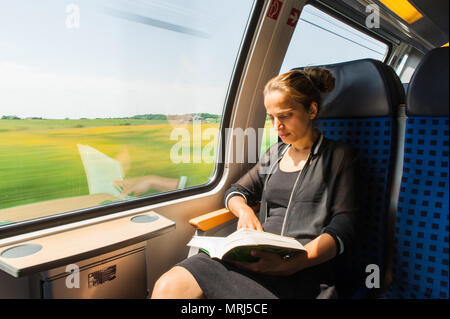 Giovane donna a leggere un libro mentre si è in viaggio in treno Foto Stock