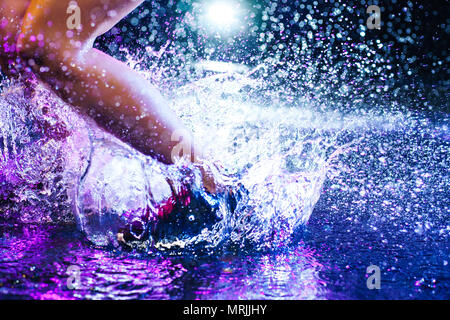 Donna che si tuffa in acqua con grandi spruzzi. Gambe e scarpe di close-up. Studio con la pioggia e le gocce interni. Foto Stock