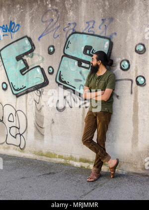 A piena lunghezza Ritratto di giovane adulto barbuto uomo indiano in posa contro il muro di graffiti, guardando lontano dalla telecamera. Foto Stock