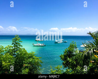 Vista Oceano con acqua turchese, piante verdi e barche sul mare, cielo blu Foto Stock