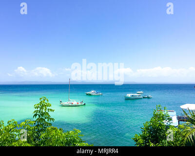 Vista Oceano con acqua turchese, piante verdi e barche sul mare, cielo blu Foto Stock
