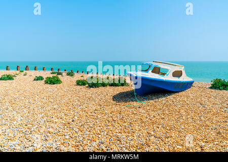 Un abbondante abbandonati barca blu su una spiaggia sassosa in Eastbourne, East Sussex, Regno Unito Foto Stock