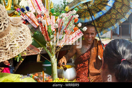 Monaco buddista in acqua imbevuto accappatoio e anta, seduti accanto a un Money Tree e sorridente a due Tailandese donne durante il Songkran 2018 Thai per i festeggiamenti di Capodanno Foto Stock