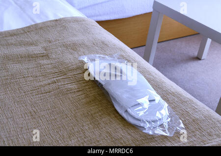 Nuovo white pantofole monouso in un imballaggio trasparente giacciono sul letto in una camera di hotel. Foto Stock