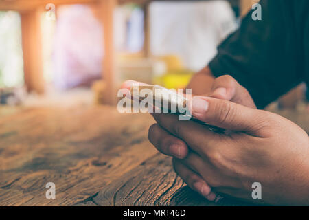 Closeup colpo di un uomo gli sms sul cellulare. Imprenditore è in possesso di un moderno smartphone e la scrittura di un messaggio telefonico al tavolo per la colazione. Mano d'uomo h Foto Stock