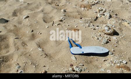 Uno bianco rotto pantofola con fascetta blu a sinistra nella sabbia Foto Stock