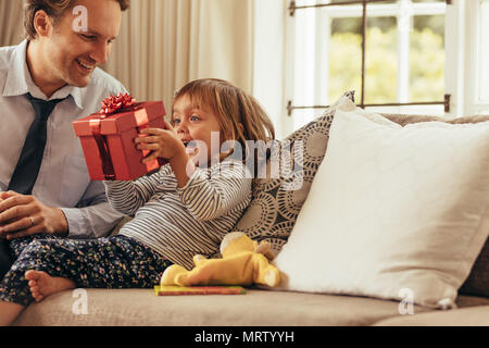 Padre e figlia seduta su un divano guardando una confezione regalo. Felice ragazza seduta con suo padre in possesso di una confezione regalo. Foto Stock