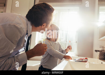 Padre e figlia spazzolare i denti in piedi in bagno e guardando ogni altro. L'uomo ad insegnare la sua figlia come spazzolare i denti. Foto Stock