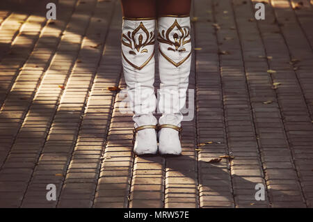 Bianco scarpe da donna sono sul marciapiede. Una ragazza in womens alta stivali da cowboy sta da solo e attende Foto Stock