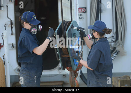 Coast Guard marinaio Lindsay Trujillo e marinaio Morgan Brooks dipingere la gru principale del blocco sul Guardacoste Ida Lewis, Mercoledì, 12 aprile 2017, a Newport, Rhode Island. Il Ida Lewis conduce ausili alla navigazione da Plymouth, Massachusetts a New Haven, Connecticut. Foto Stock