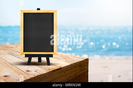 Lavagna vuota sul tavolo in legno stand alimentari con blur spiaggia di sabbia e il mare blu con bokeh sfondo luminoso.Modello Mock up per la vacanza estiva promozione Foto Stock